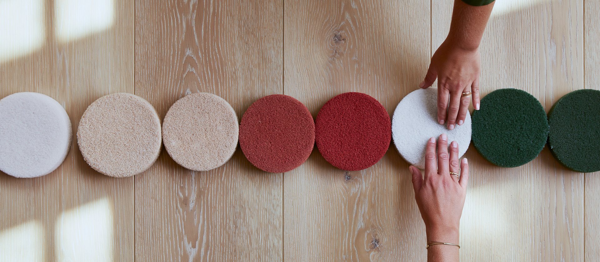 Reihe runder Pads in Weiß, Beige, Rot und Grün, Hände sortieren auf hellem Holzboden